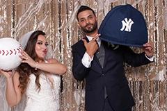 The Bride and Groom posing for photos on the Mirror Me, with their guests, in front of a backdrop, holding signboards and props