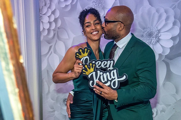 Elegant Black couple. Man kisses woman holding "Queen" and "King" signs at an event.